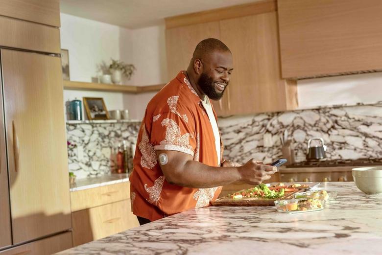 A man standing in a kitchen using his phone to take photos of the meal he is preparing
