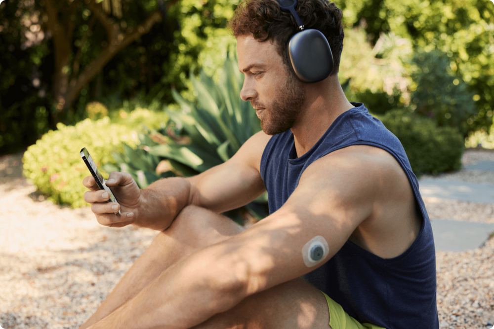 Man sitting down outside on his phone while wearing the Stelo sensor