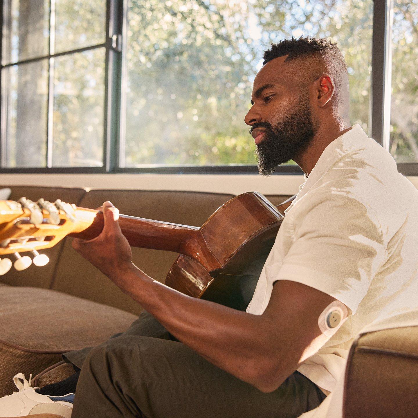 Man playing guitar, wearing Stelo glucose sensor on the back of his arm