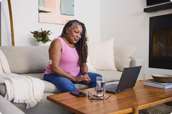 Woman sitting on couch wearing Stelo smiling at laptop