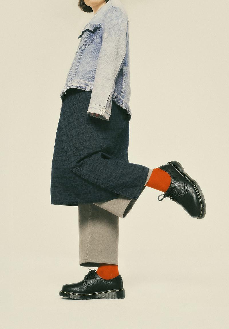 Black leather lace-up shoes with yellow welt stitching, worn with bright orange socks