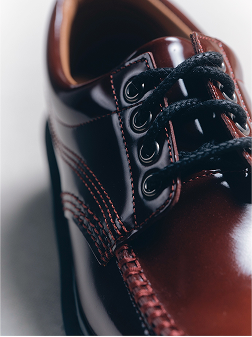 Primer plano de zapato de charol burdeos con cordones negros y costuras rojas