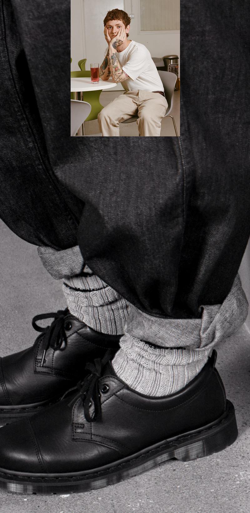 Zapatos de cordones de piel negra con calcetines acanalados grises y vaqueros negros enrollados