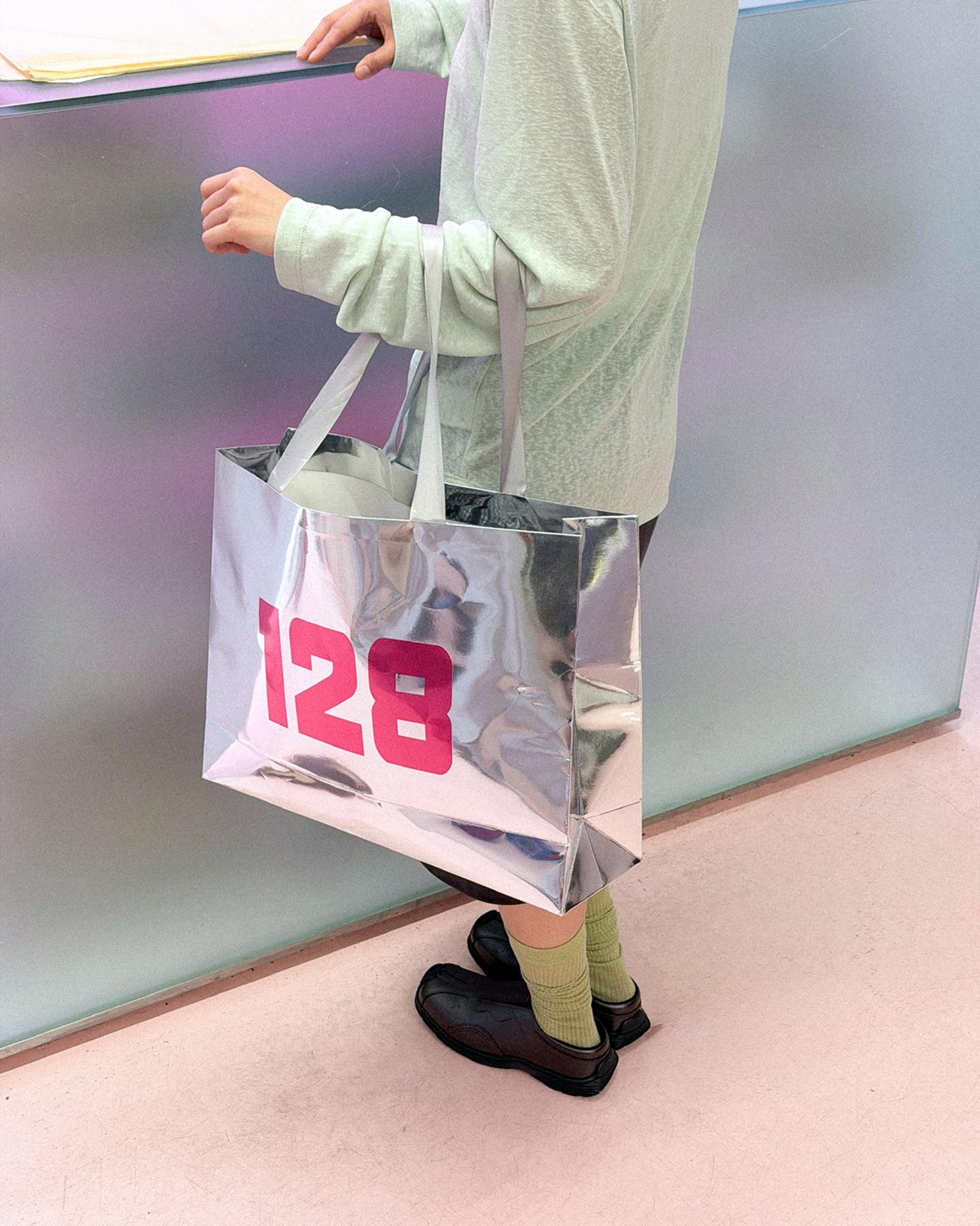 Silver tote bag with pink 128 print, carried by hand
