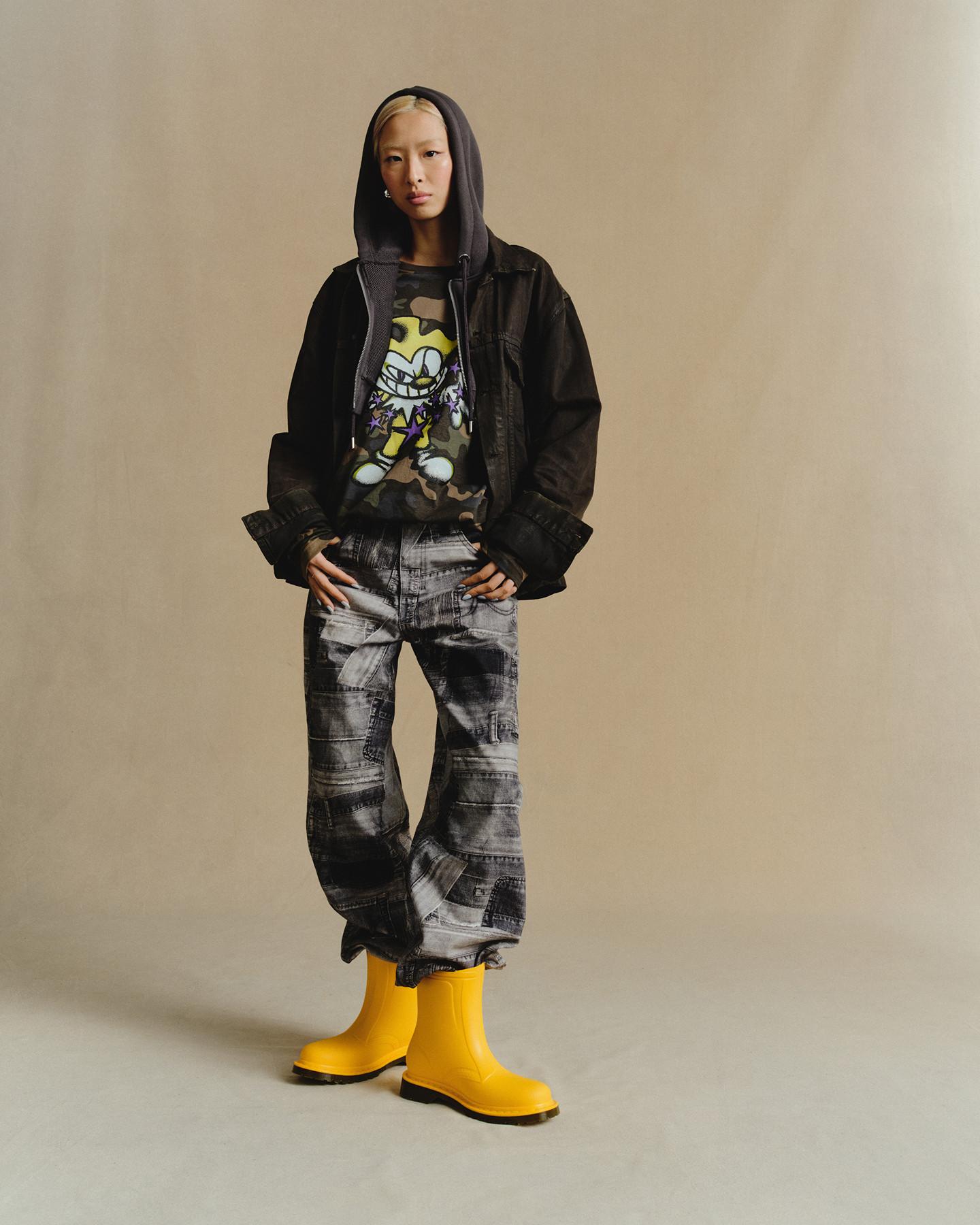 Persona con botas de goma amarillo vivo, chaqueta negra y sudadera gris sobre camiseta camuflaje