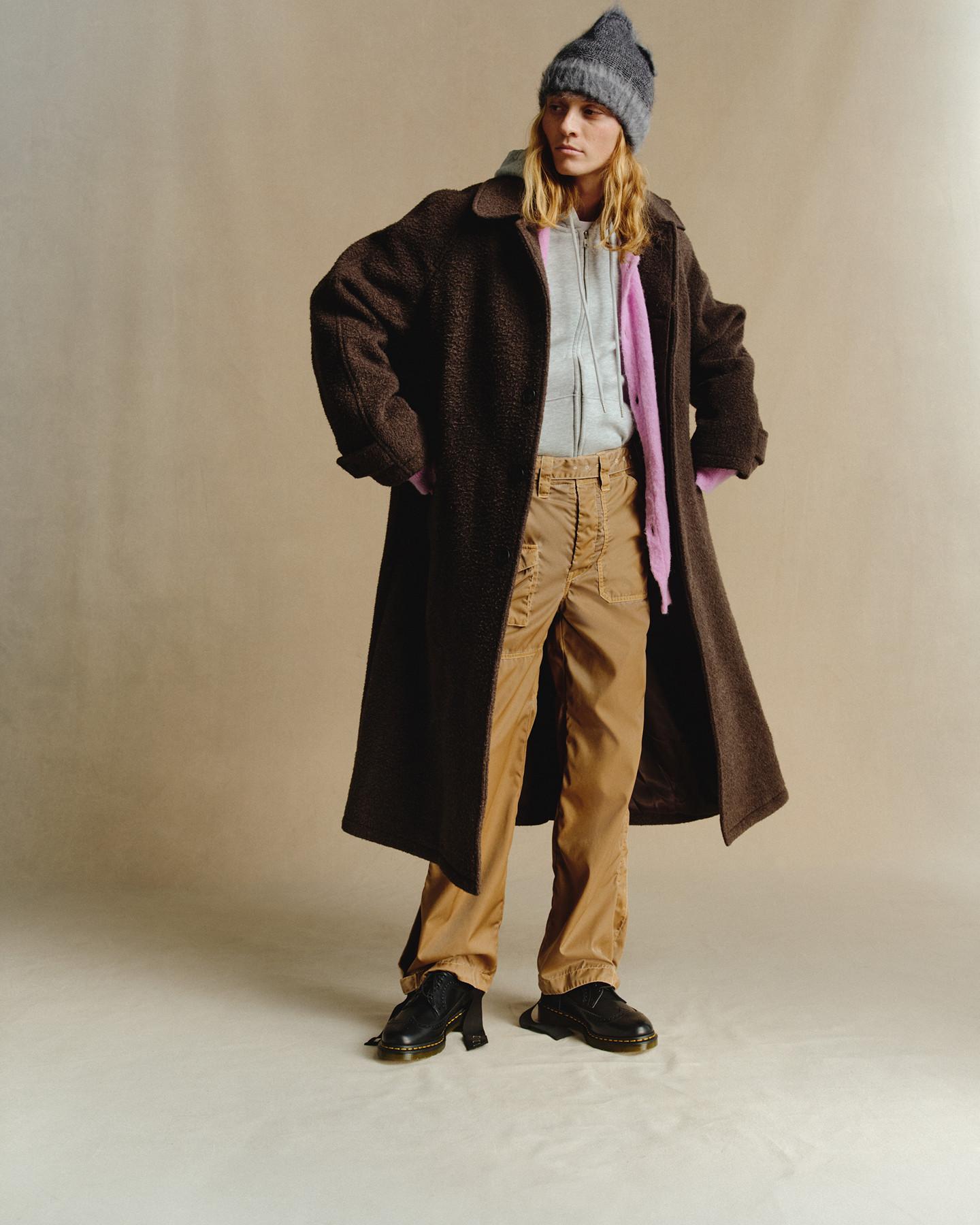 Black leather heeled loafers worn with beige trousers and an oversized brown coat