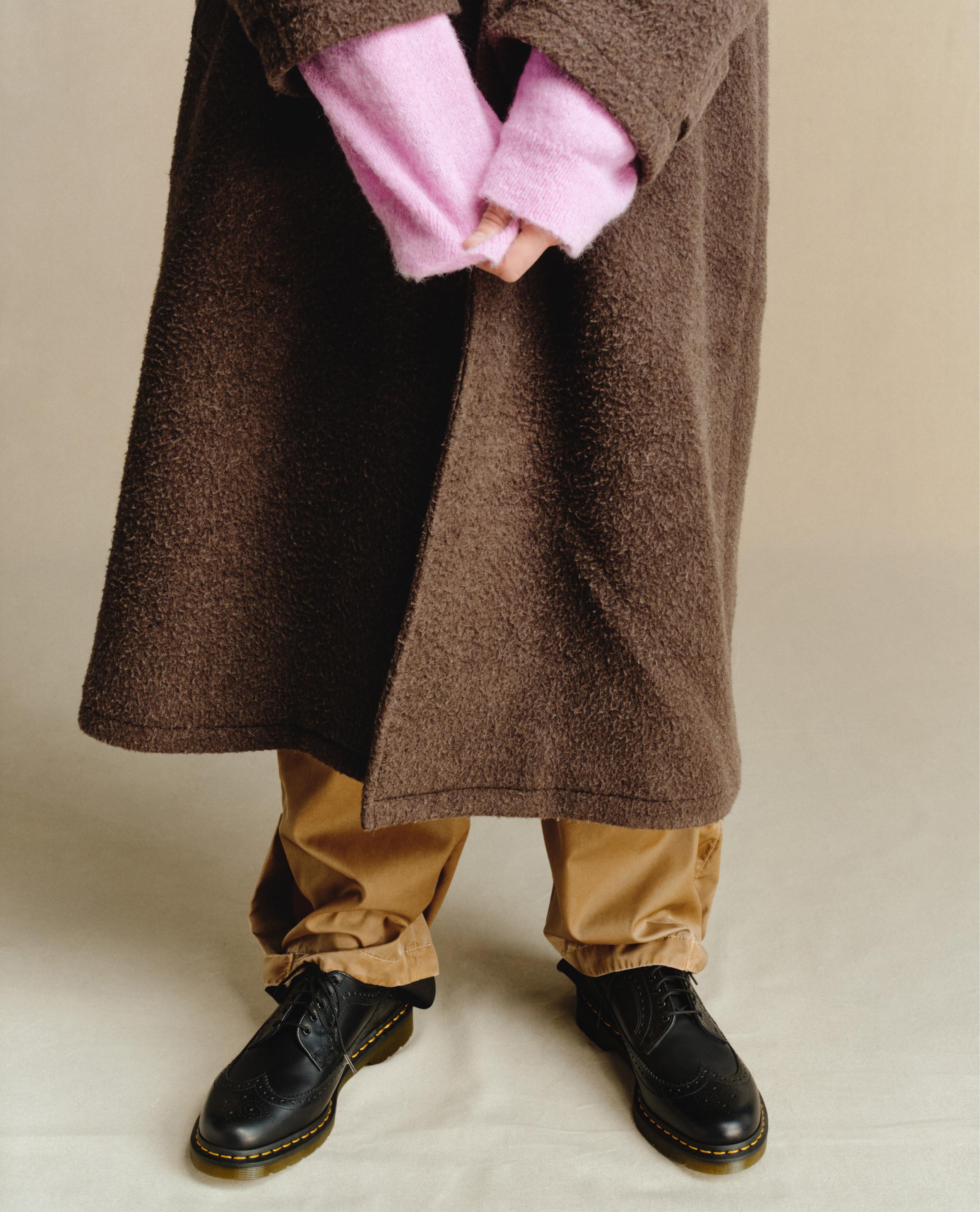 Black leather brogue shoes with yellow welt stitching, worn with tan trousers and a brown coat