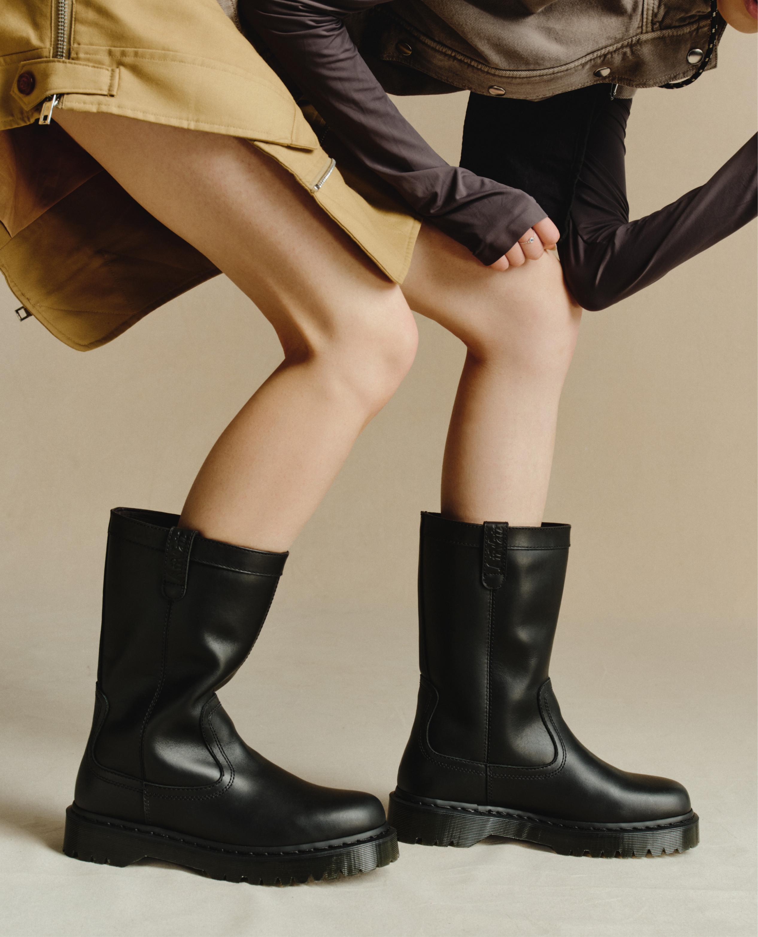 Two people in black leather mid-calf boots with chunky soles, crouched in skirts