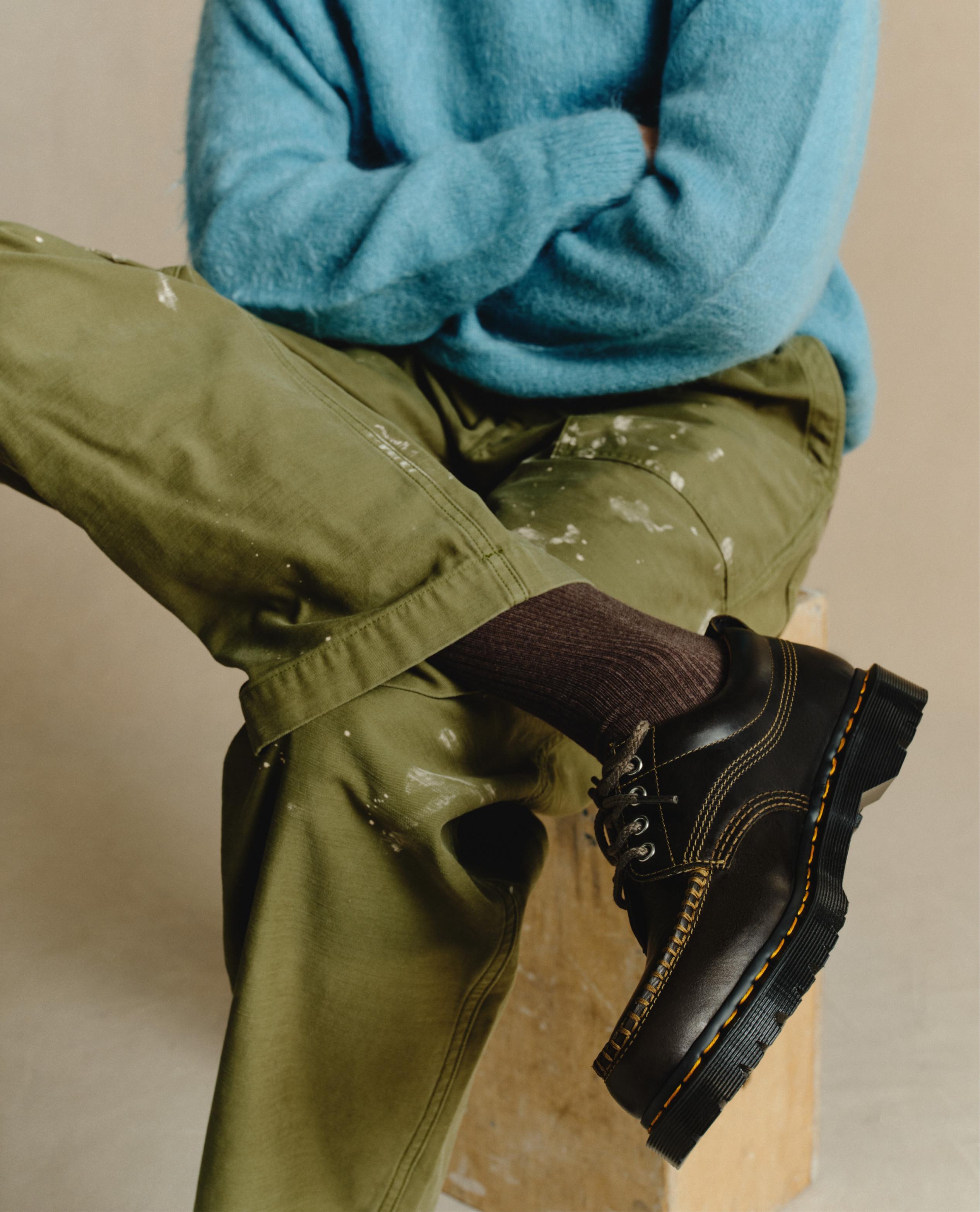 Black leather lace-up shoes with yellow welt stitching, worn with khaki paint-splattered trousers