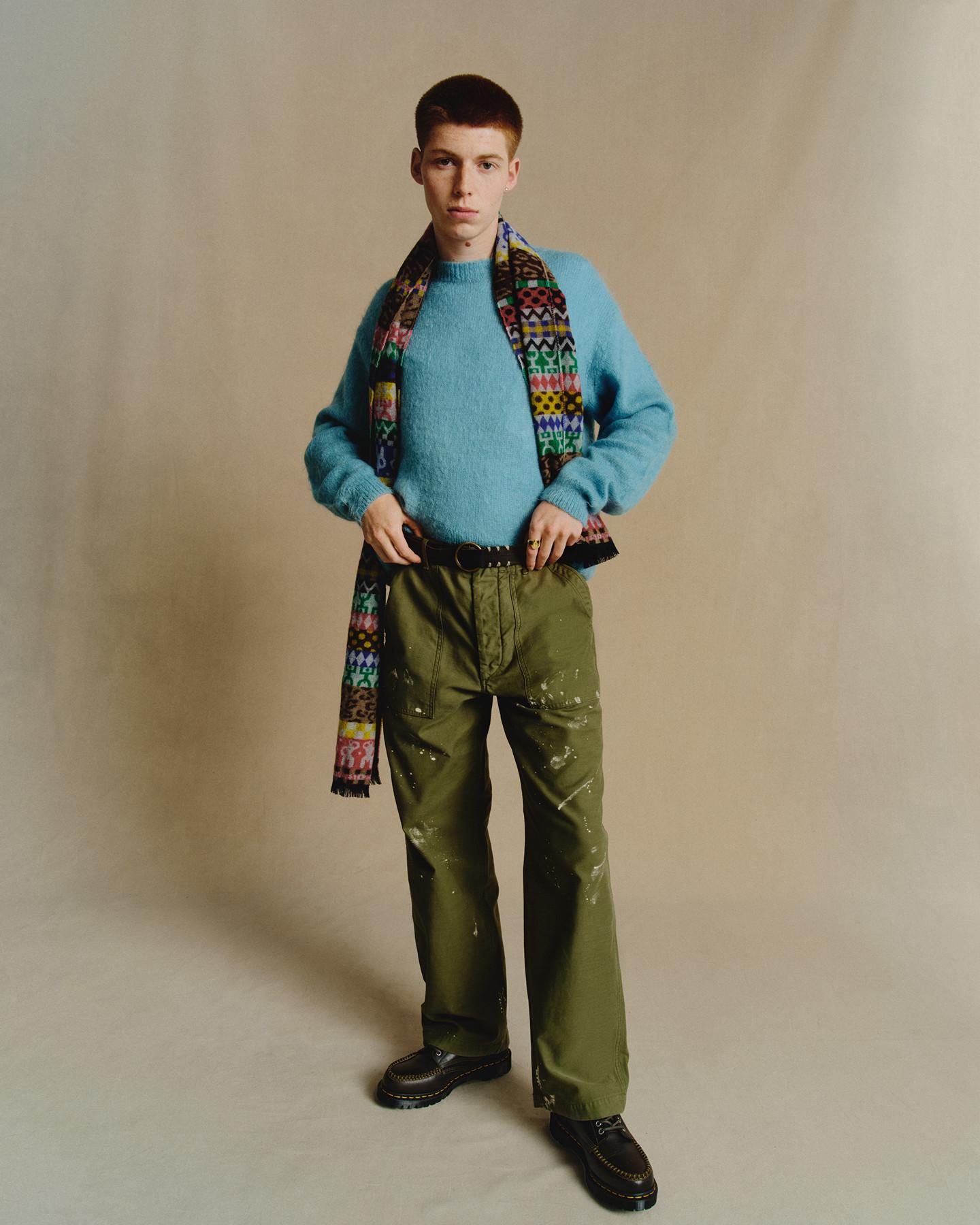 Black leather loafers with yellow welt stitching, worn with olive trousers and a bright blue jumper