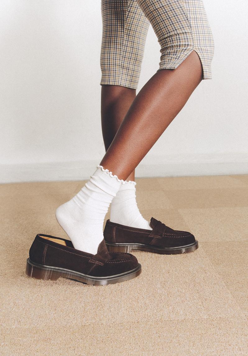 Person in black leather loafers with white socks, shorts and a checked shirt tied at the waist