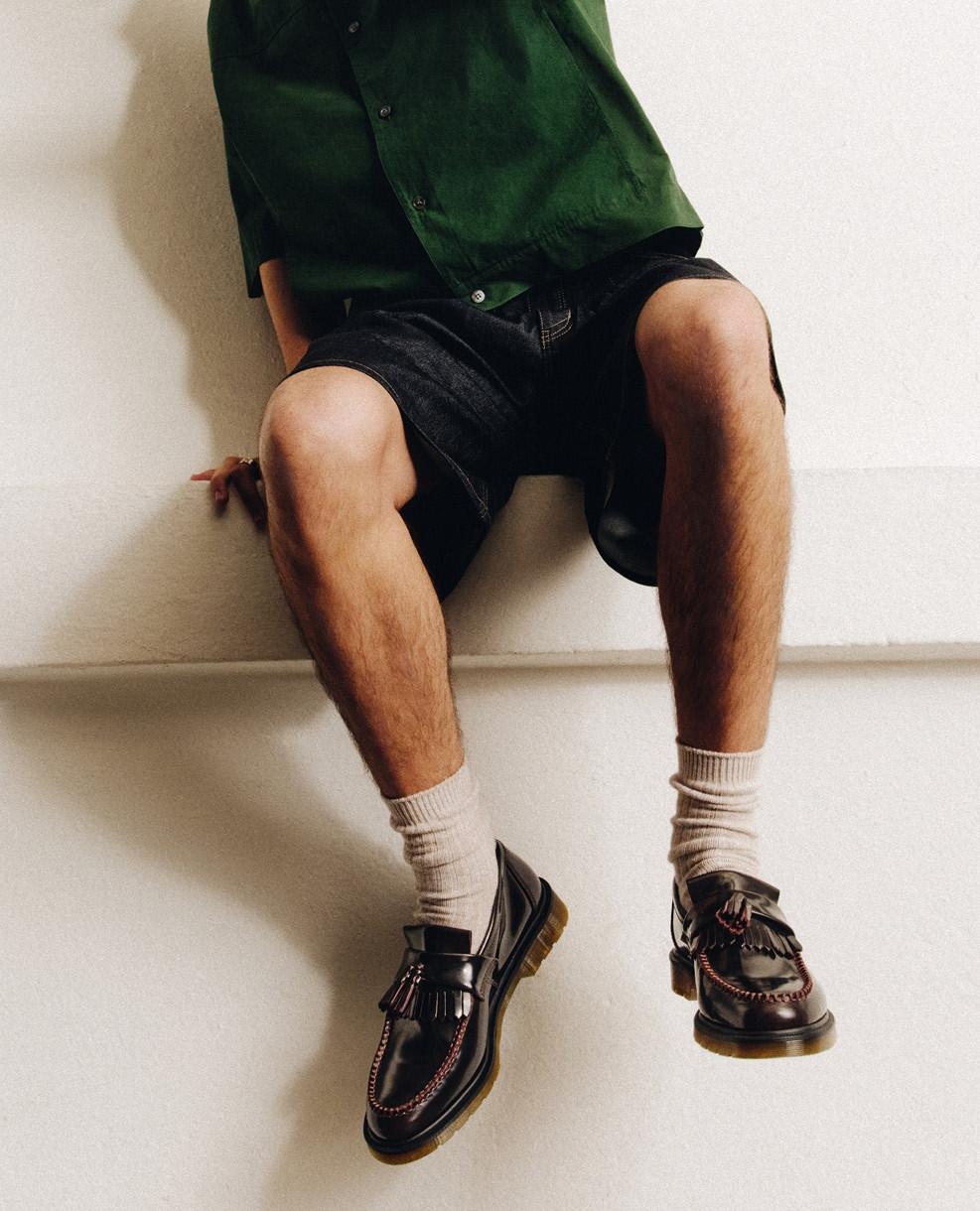 Black leather tassel loafers with welt stitching, worn with cream ribbed socks