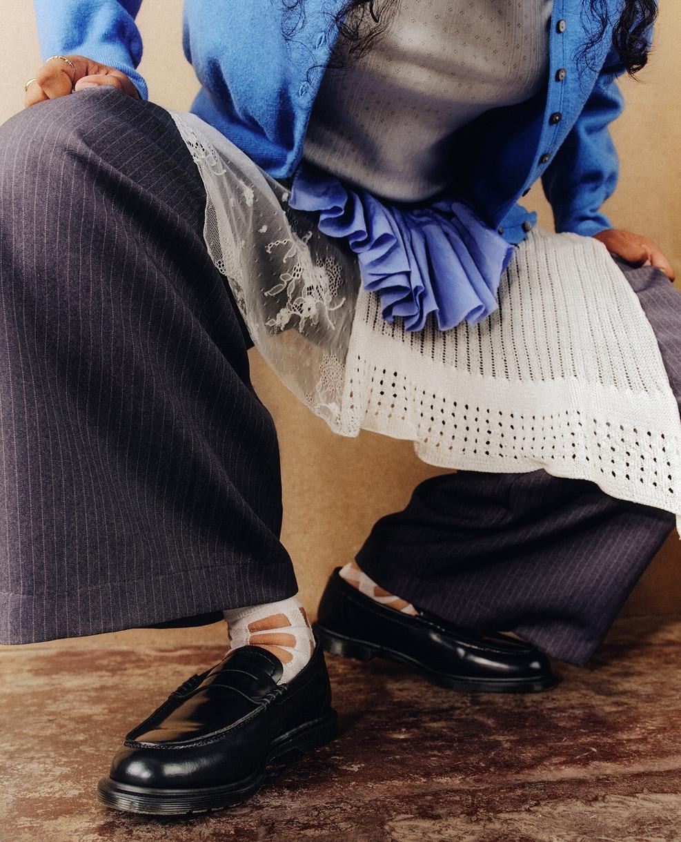 Black leather loafers with white cutout socks, worn with pinstripe trousers and layered lace skirt