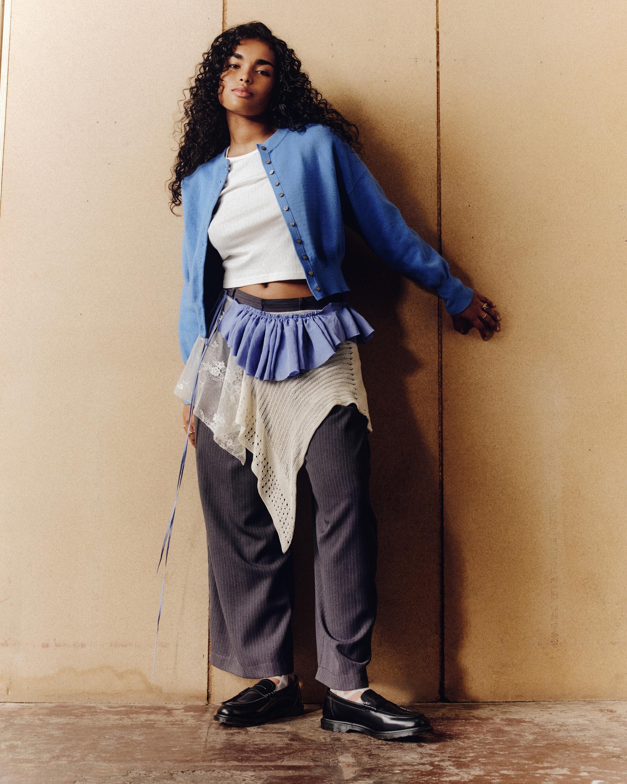 Person in black leather loafers with white socks, blue cardigan and layered skirt panels