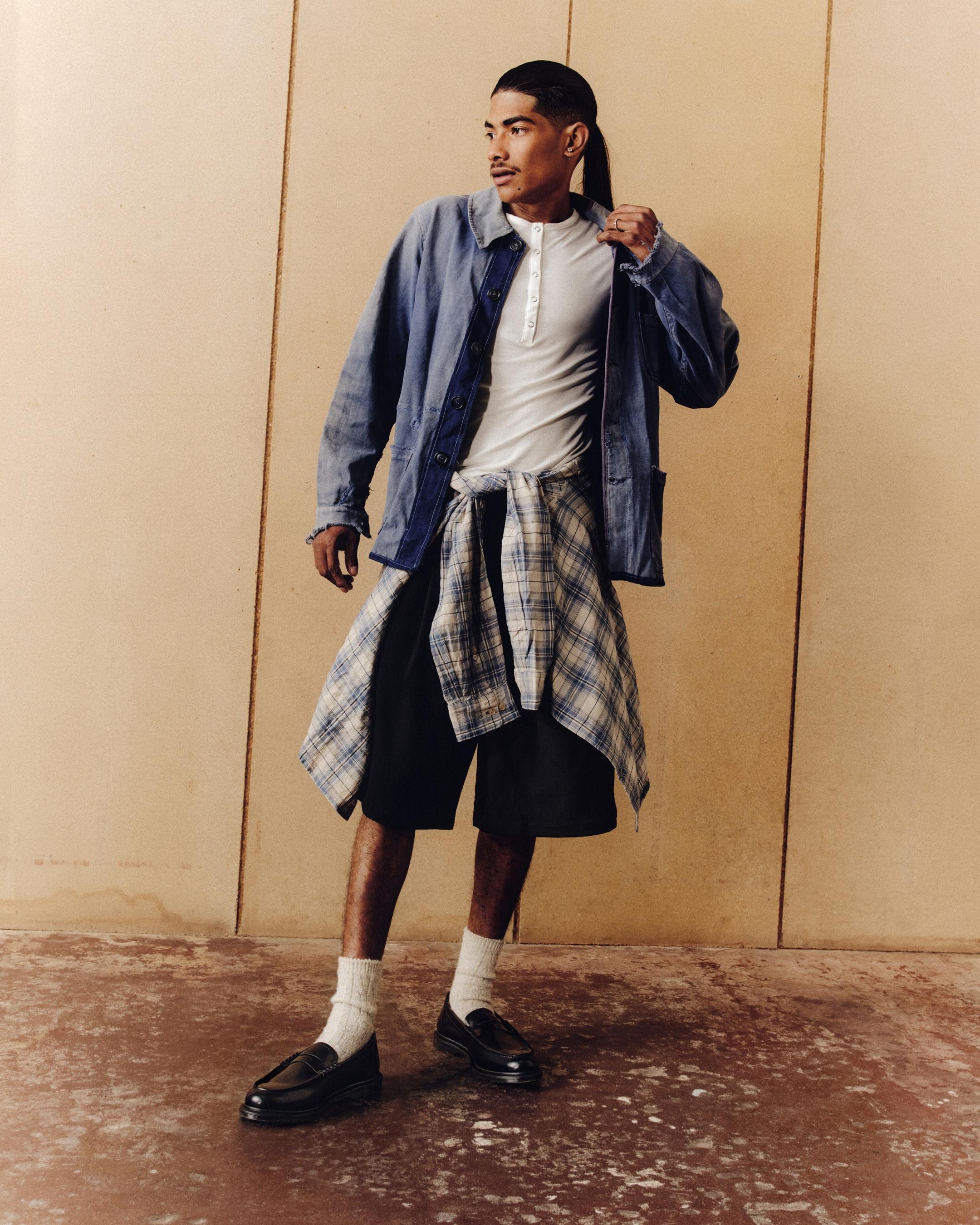 Person in black leather loafers, white socks and shorts, with a checked shirt tied at the waist
