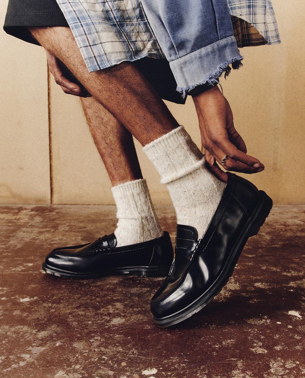 Black leather loafers with off-white ribbed socks, worn with rolled-up trousers