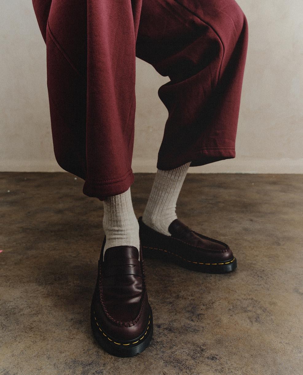 Burgundy leather loafers with yellow welt stitching, worn with grey ribbed socks and maroon trousers