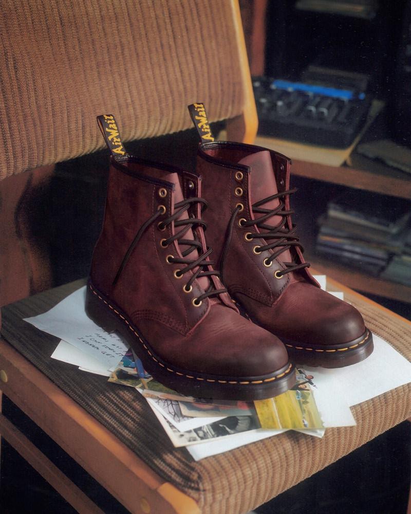 Burgundy leather lace-up boots with yellow welt stitching, resting on scattered postcards