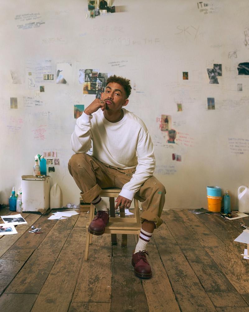 Person in burgundy leather shoes, striped socks and paint-splattered trousers on a studio stool