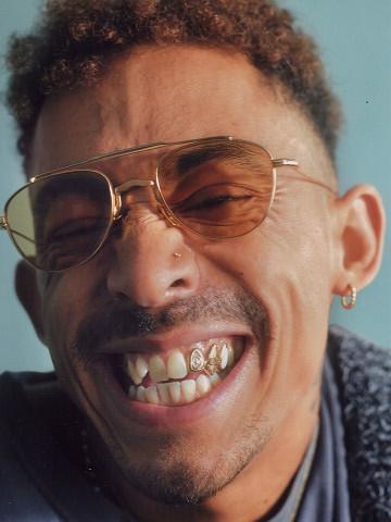 Close-up of a person grinning in gold aviator sunglasses, showing a gold tooth cap