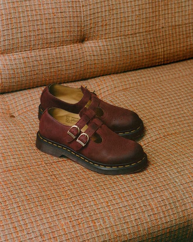 Burgundy leather Mary Jane shoes with double buckles and yellow-stitched sole on a sofa