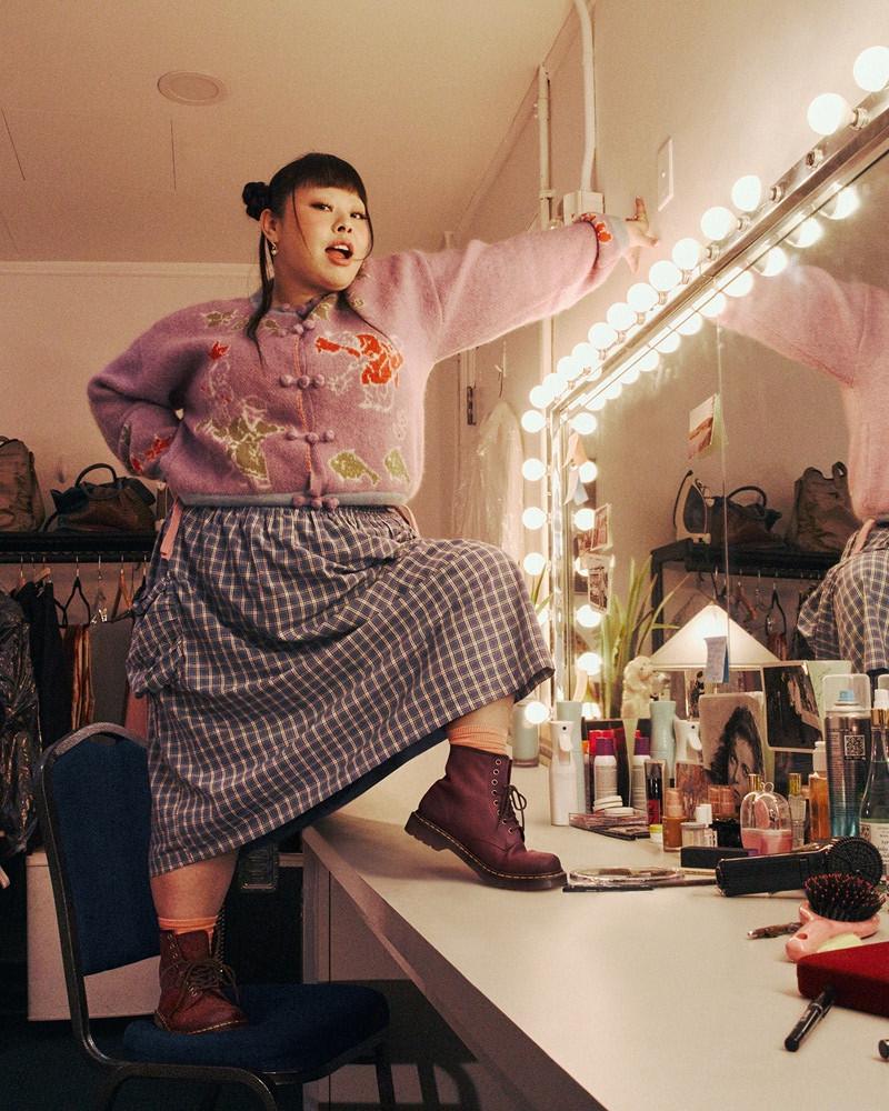 Person posing in burgundy lace-up boots on a dressing-room vanity lit by bulb mirror