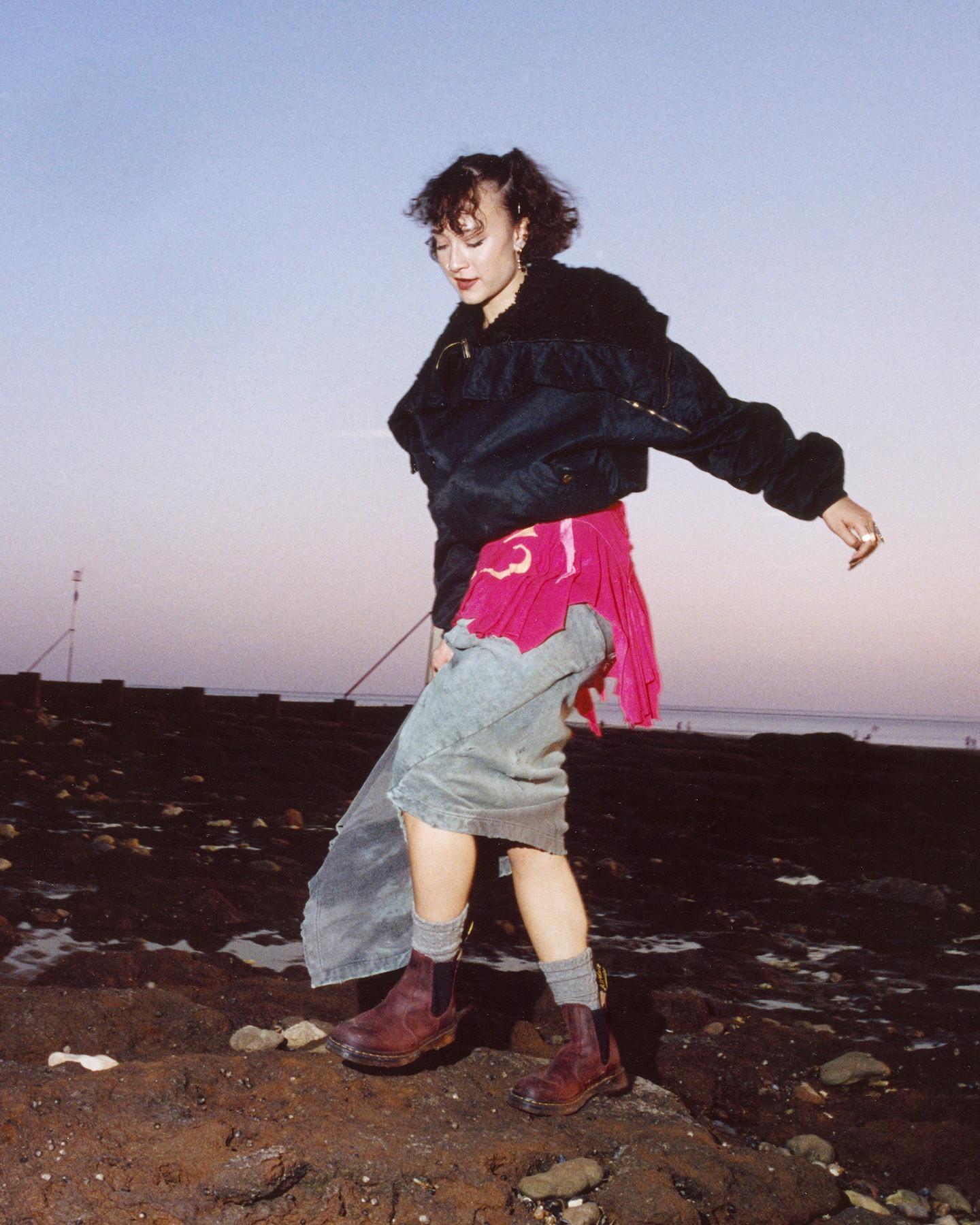 Bordeauxröda Chelsea-boots med grå strumpor på en klippig strand i skymningen