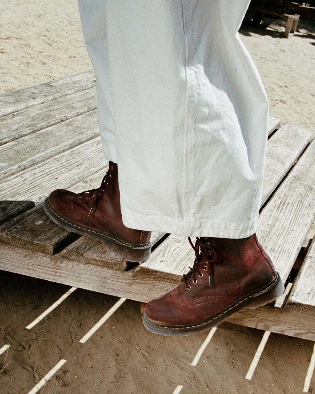 Worn-in dark brown leather lace-up boots with yellow welt stitching, under white trousers