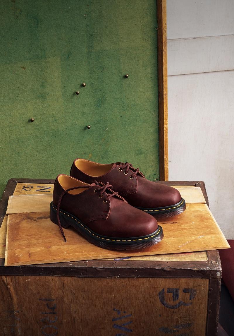 Chaussures 3 œillets en cuir rouge cerise avec surpiqûres jaunes sur une caisse en bois