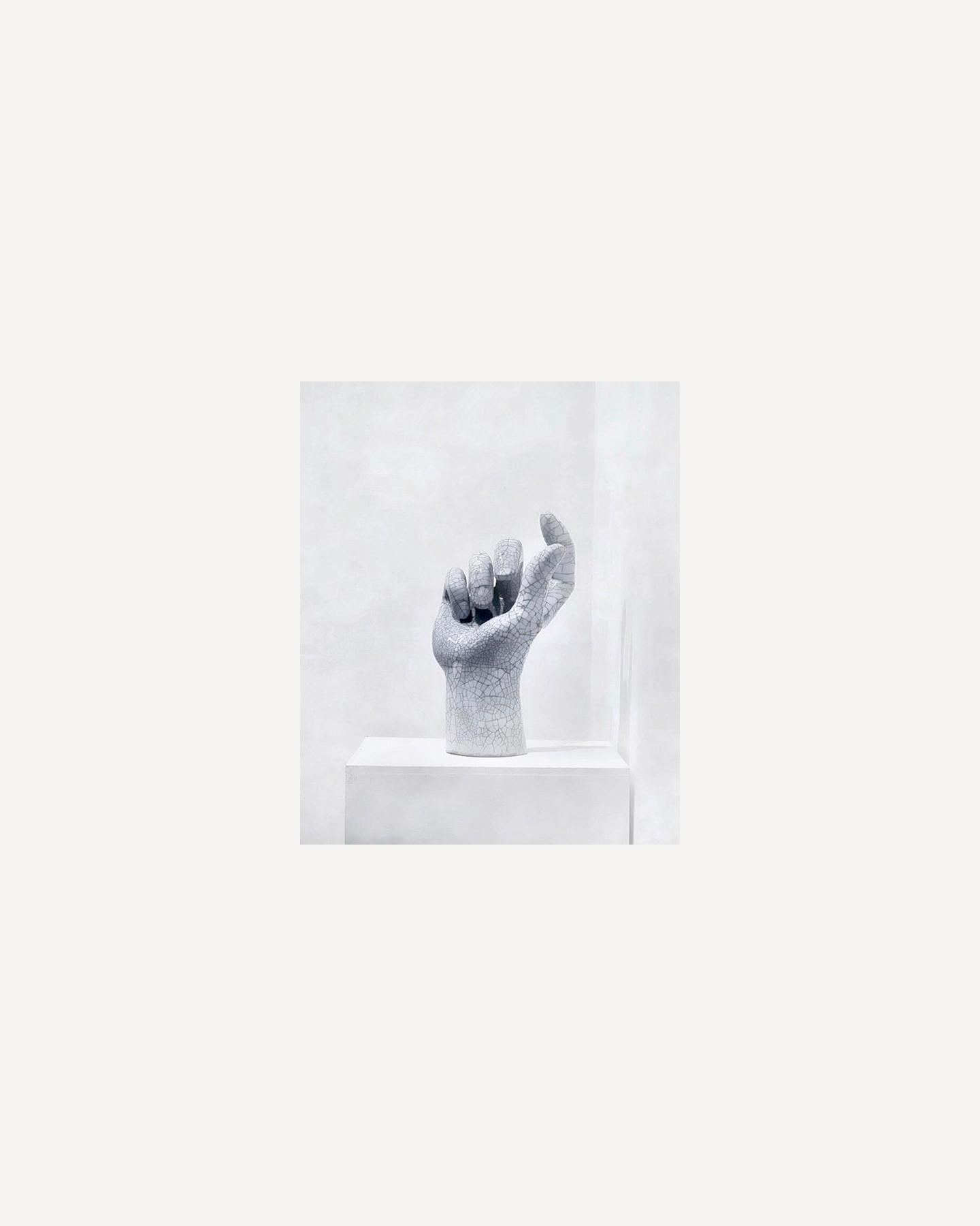 White ceramic hand sculpture with crackle glaze on a white plinth