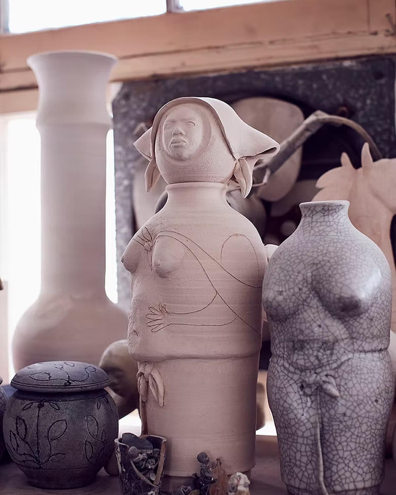 Handmade ceramic vases and sculpted figures on a workbench, dusty clay and crackle glaze