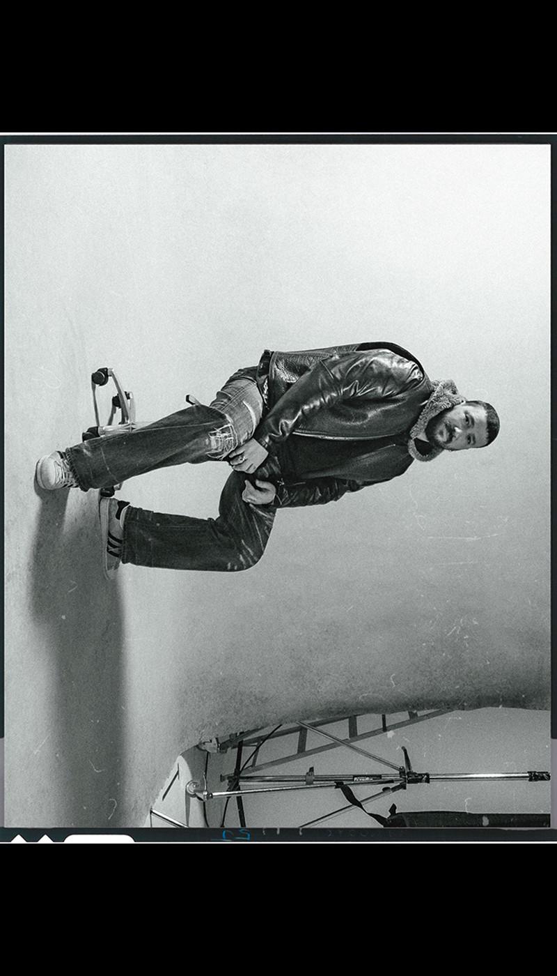 Black-and-white studio shot of a person in a shearling-collar leather jacket and jeans