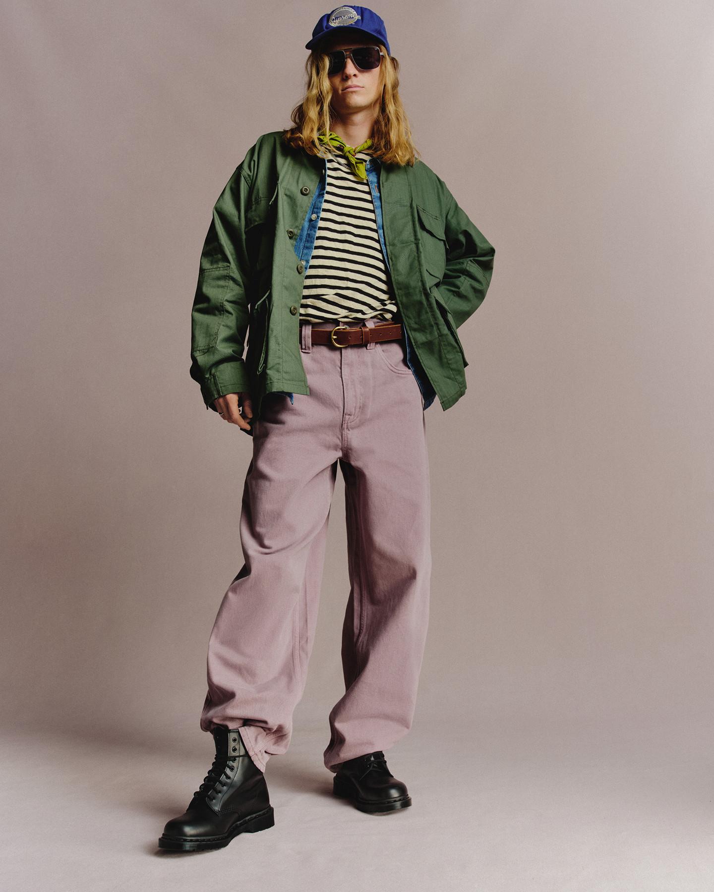 Person in black leather lace-up boots, lilac trousers and green jacket with striped tee