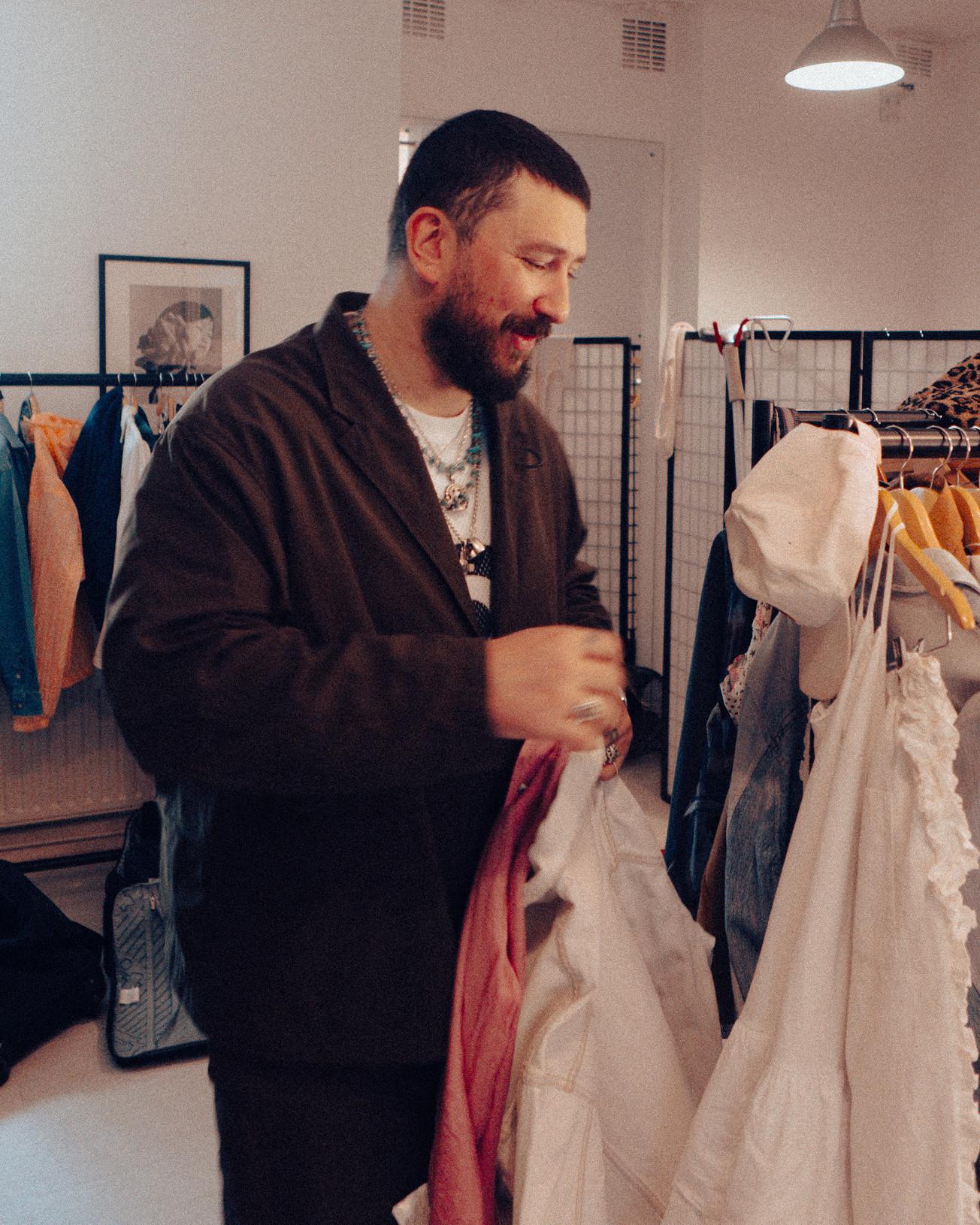 Person in a dark coat flicking through clothes on a rail in a studio