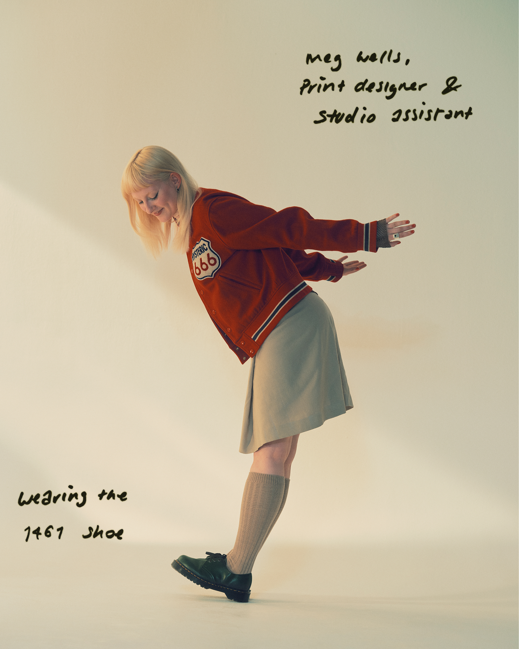 Person in red varsity jacket and grey skirt, leaning forward in black 1461 shoes