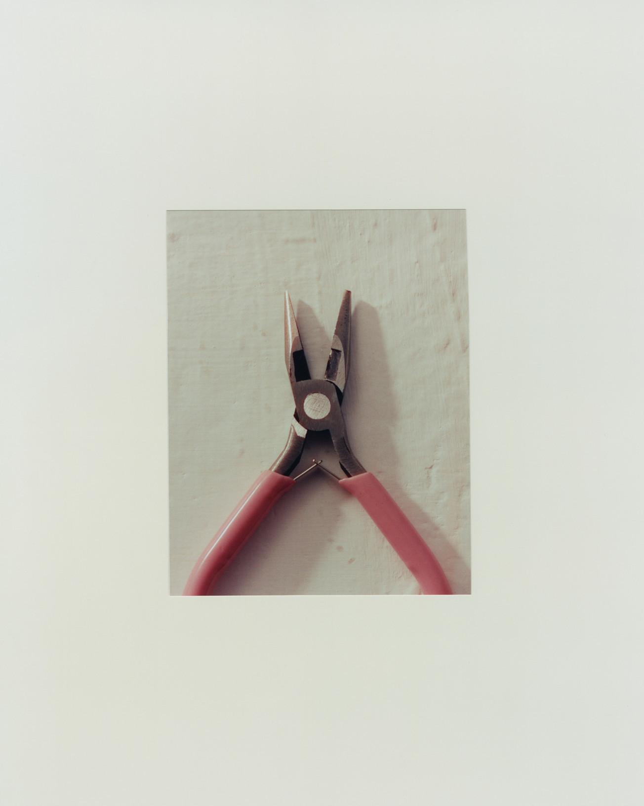 Red-handled metal pliers on a pale, worn tabletop