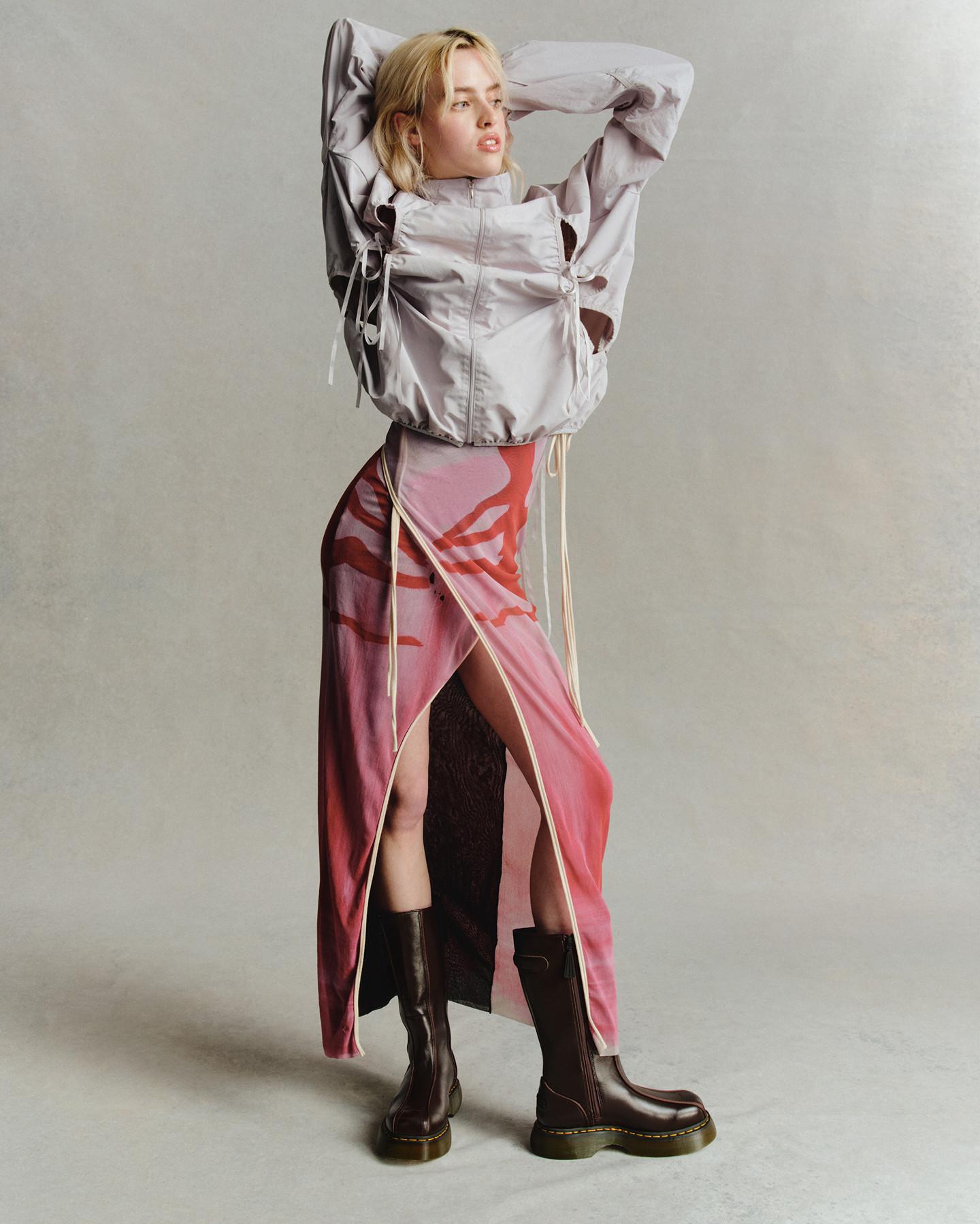 Persona con botas de cuero marrón oscuro con cremallera, falda rosa con abertura y chaqueta gris claro