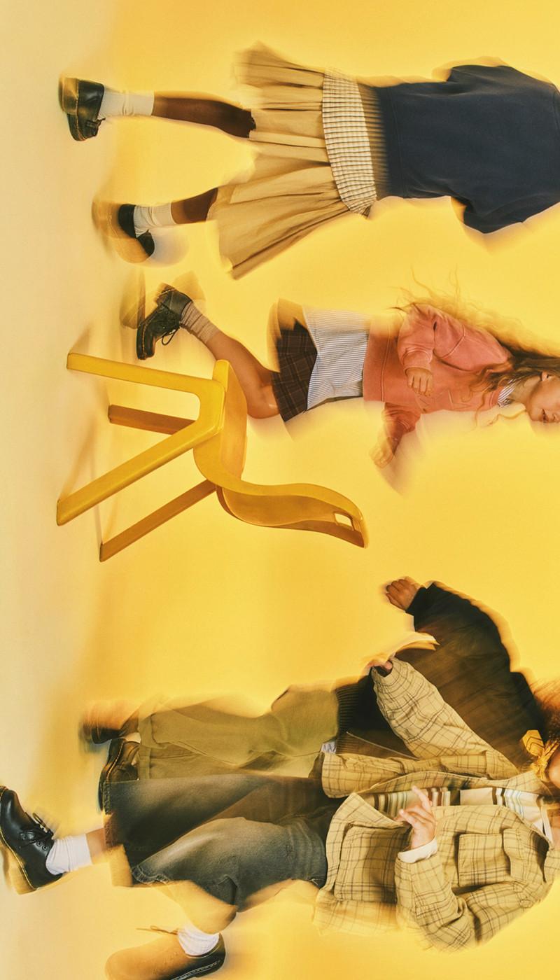 Three kids in black lace-up Docs on a yellow floor, motion blur and tipped yellow chair
