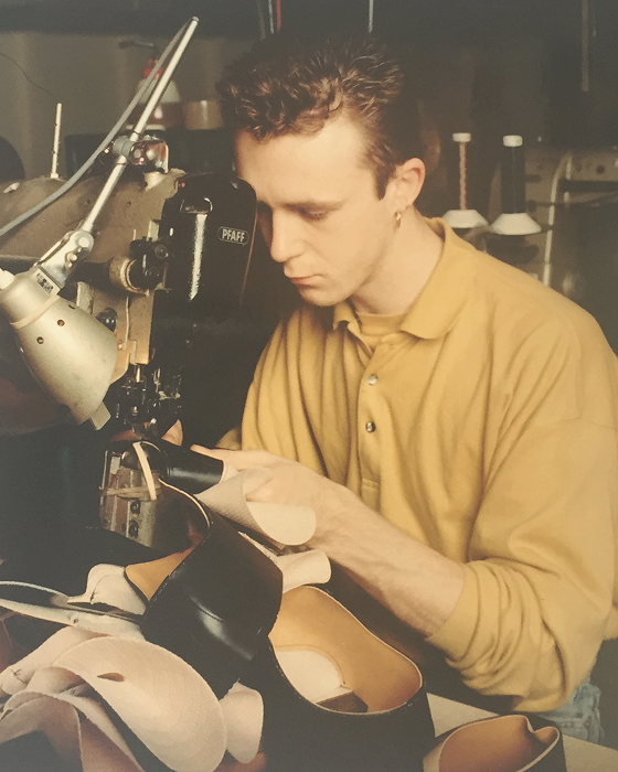 Schuhmacher in senfgelbem Polo näht schwarzes Leder an einer Industriemaschine