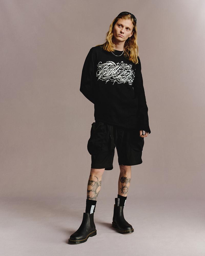 Person in schwarzem Print-Sweatshirt, Cargoshorts und schwarzen Chelsea-Boots mit gelber Naht