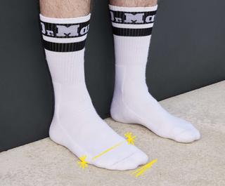 Un paio di piedi in calzini bianchi con un segno giallo simile a una penna sul piede destro, che mostra il punto migliore per misurare il numero di scarpe