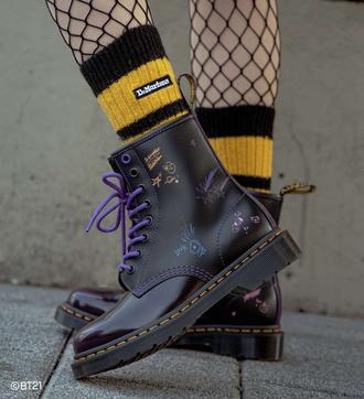 Bottes Dr. Martens noires avec motifs violets, chaussettes rayées jaunes et noires.
