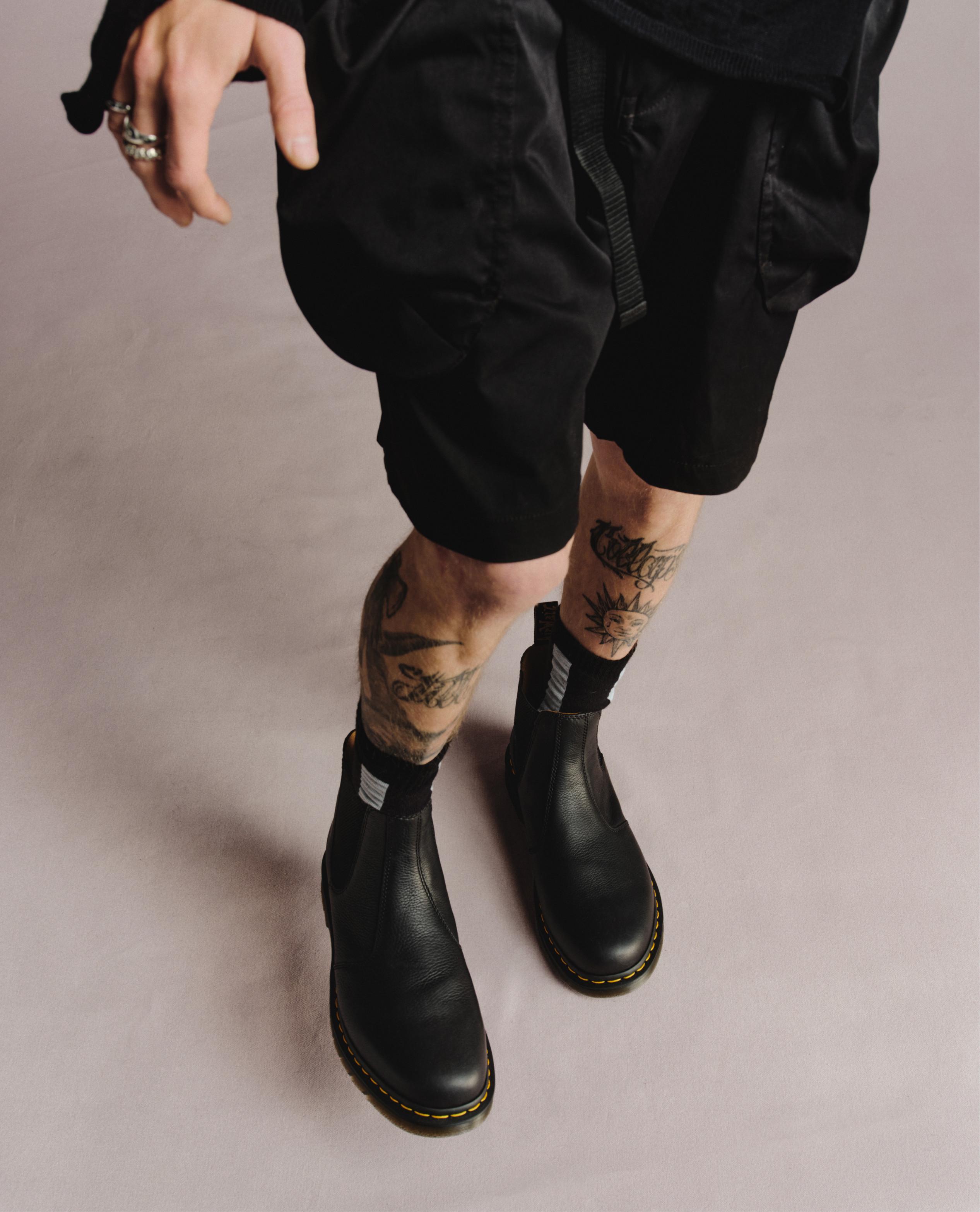 Black leather Chelsea boots with yellow welt stitching, worn with black shorts and striped socks