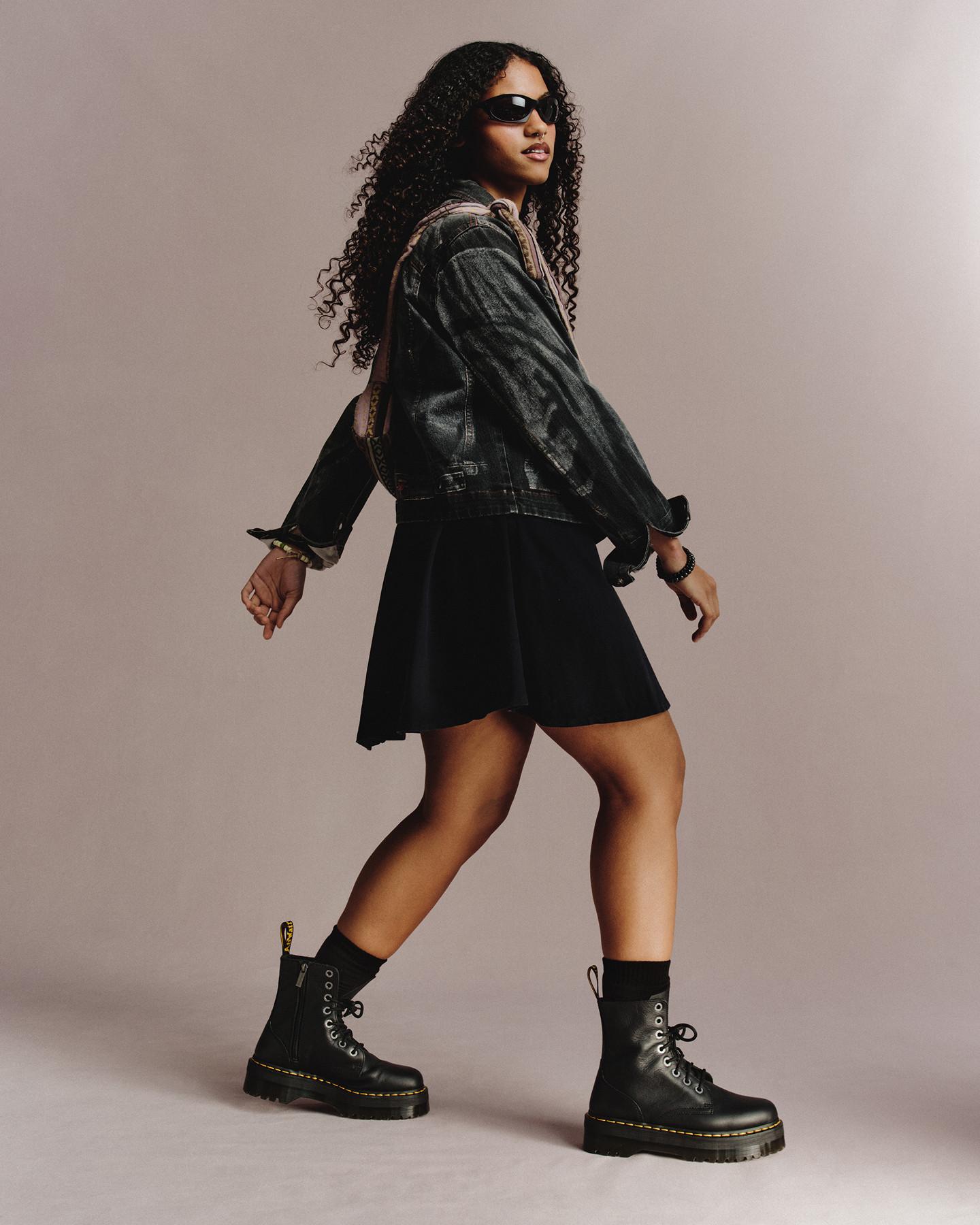 Person in black leather 8-eye boots, denim jacket and skirt, walking in studio