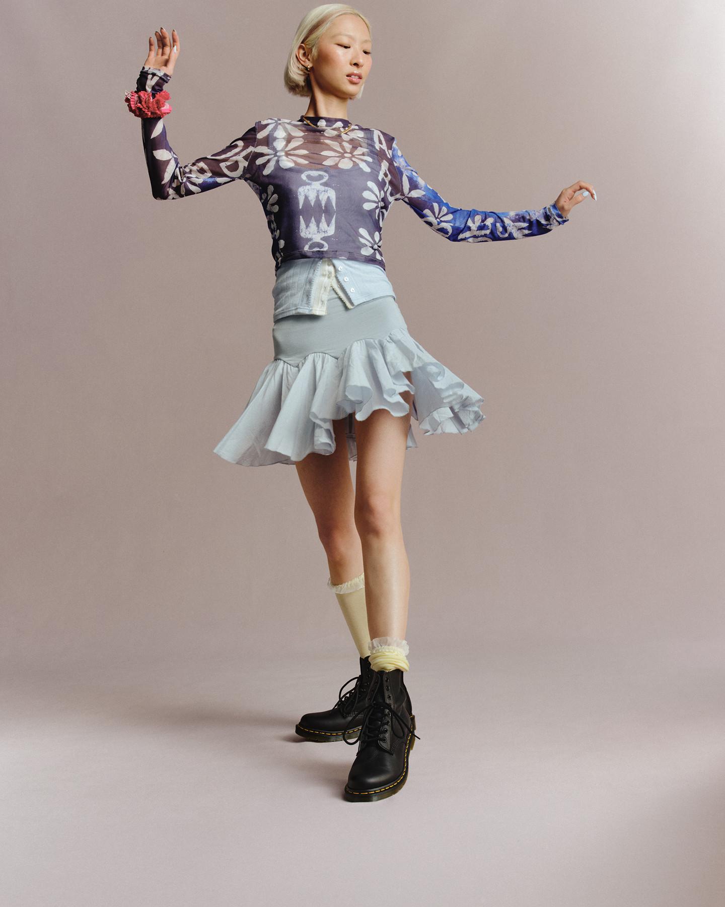 Person in black leather lace-up Docs with yellow welt stitch, sheer floral top and ruffled skirt