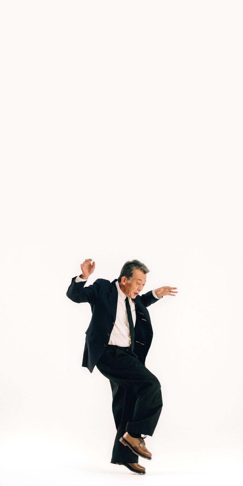 Person in a black suit mid-step in tan leather shoes against a white studio backdrop
