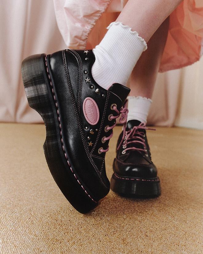 Black leather platform shoes with pink laces and star studs, worn with white frill socks