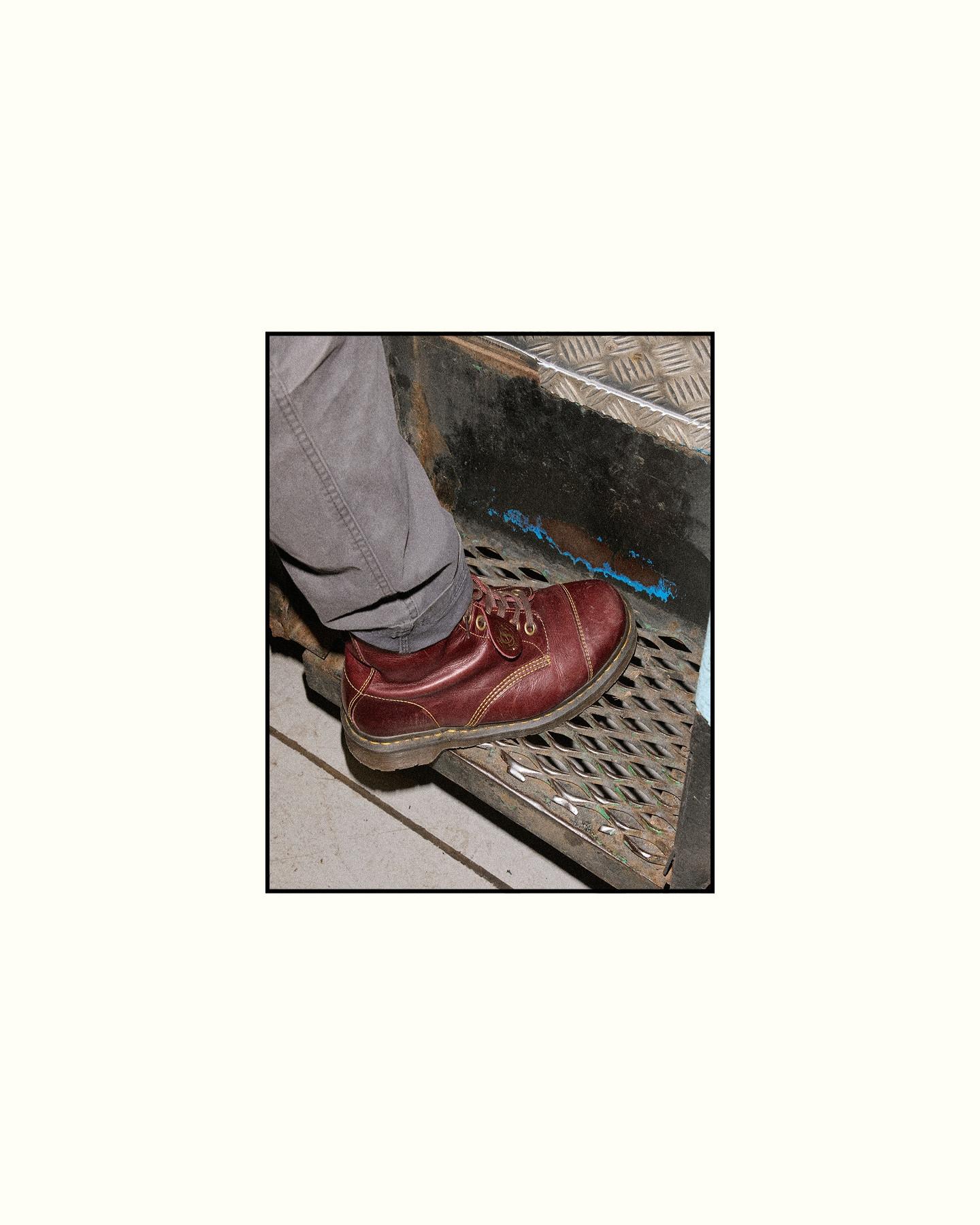 Worn burgundy leather lace-up shoe on a metal grate step, grey trouser leg