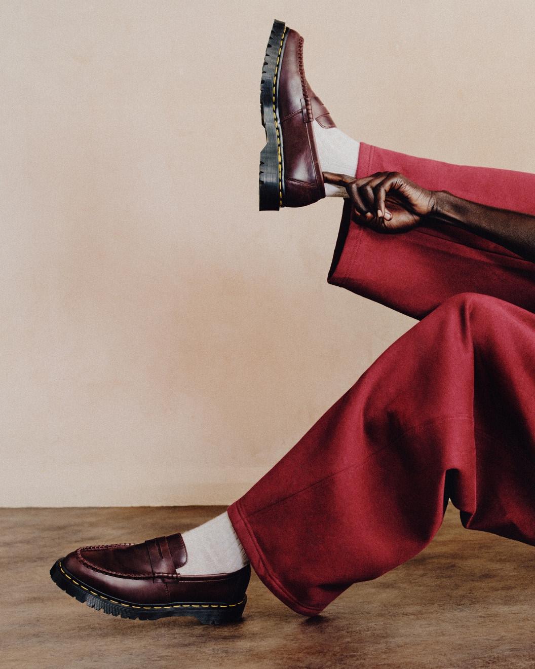 Burgundy leather loafers with yellow welt stitching, worn with white socks and wide red trousers