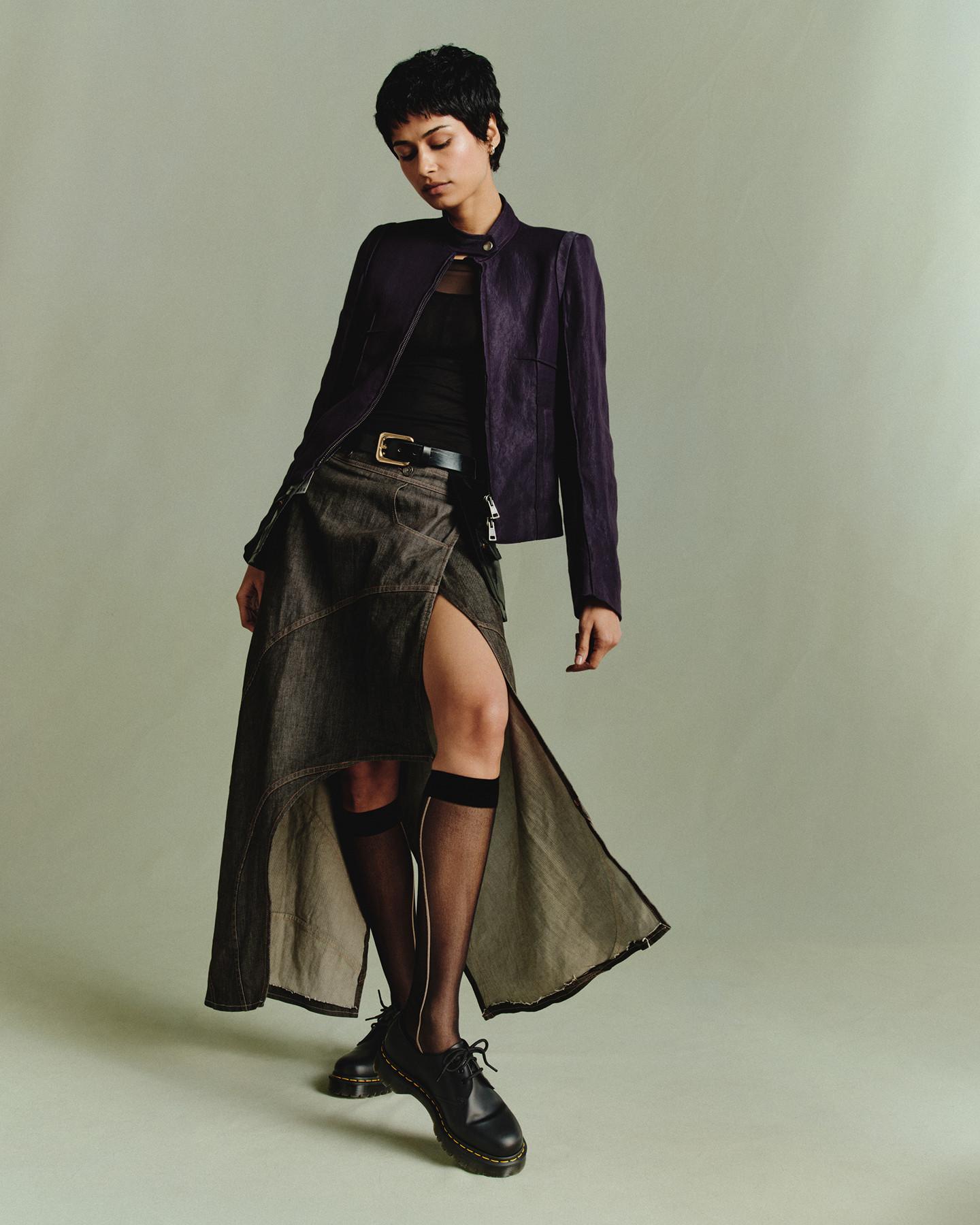Persona con zapatos negros de piel de 3 ojales, calcetines transparentes a la rodilla y chaqueta morada, falda larga